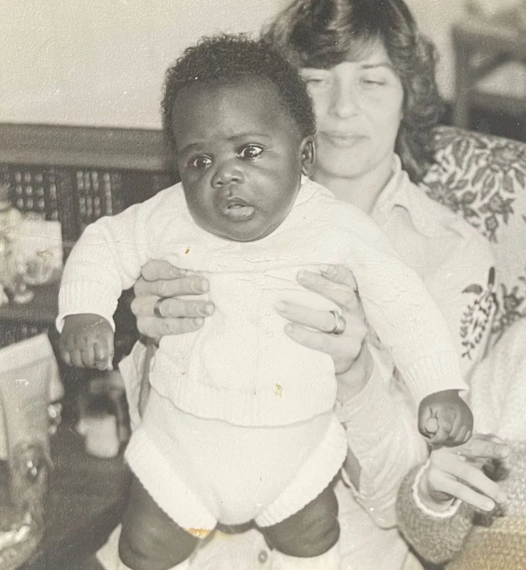 Peter as a baby, held up by a woman, with a young boy beside them